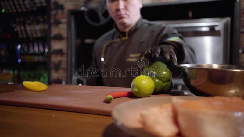 Шеф-повар портрета прерывая с зеленым цветом острого ножа и желтым болгарским перцем на деревянной доске для подготовки салата в